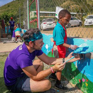A volunteer and young survivor working together to paint the outside of a school in the British Virgin Islands