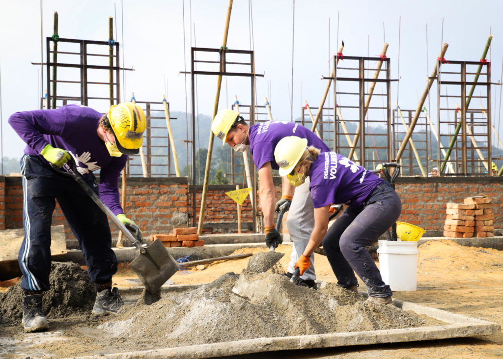 three volunteers mixing concrete with shovels