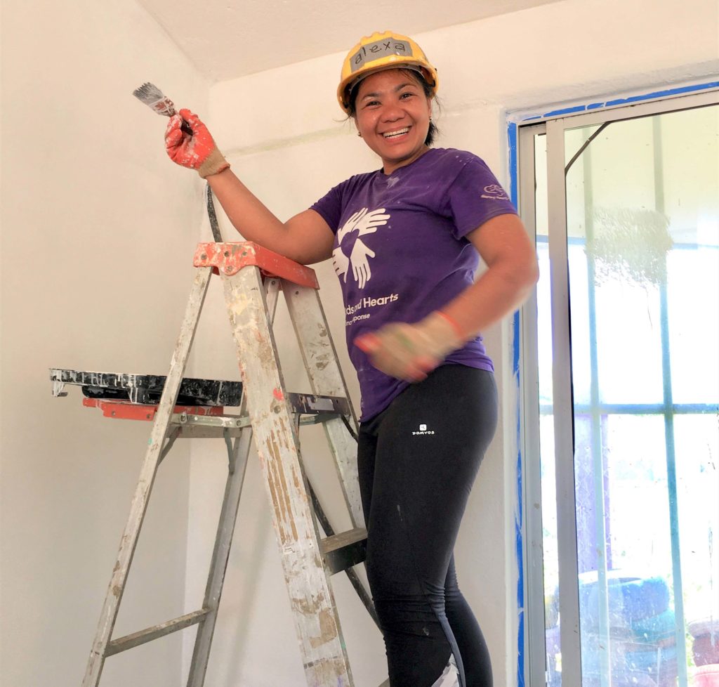 a volunteer on a ladder with a paint brush smiling
