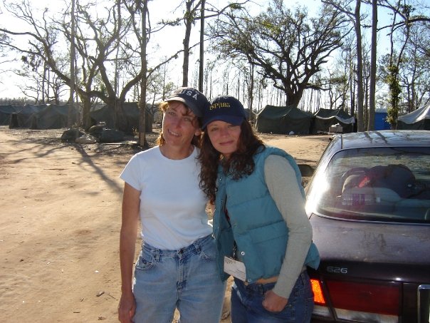 Dos mujeres de pie y sonriendo junto a un coche en el exterior.