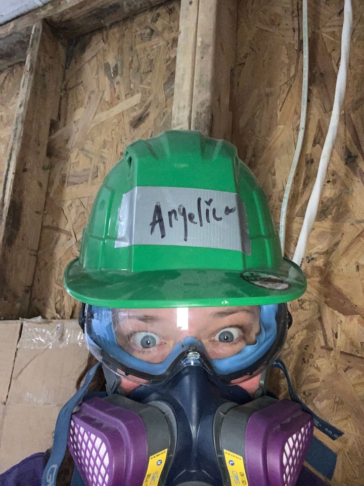 Women with face mask and green hard hat doing construction inside a house. 