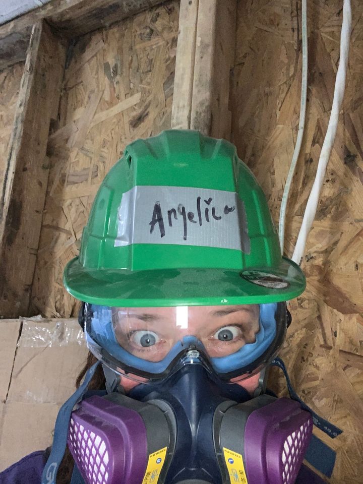 Mujer con mascarilla y casco verde haciendo obras en el interior de una casa. 