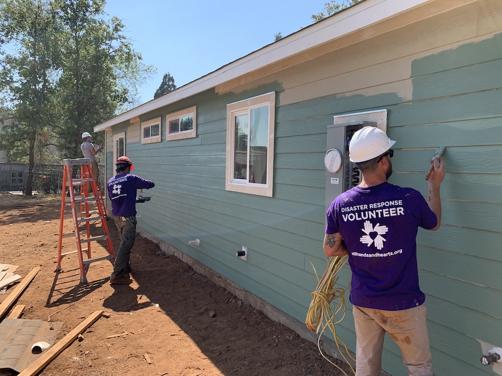 Voluntarios pintando una casa con pintura azul. 