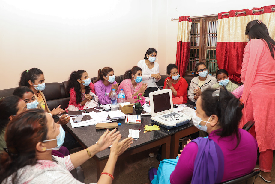 Las mujeres nepalíes con máscaras se reúnen alrededor de una mesa para asistir a los cursos de formación. 