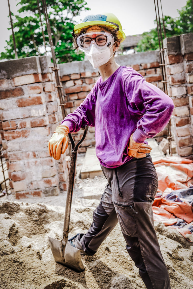 Nepal volunteer standing with a shovel, mask and goggles on in a pile of dirt. 