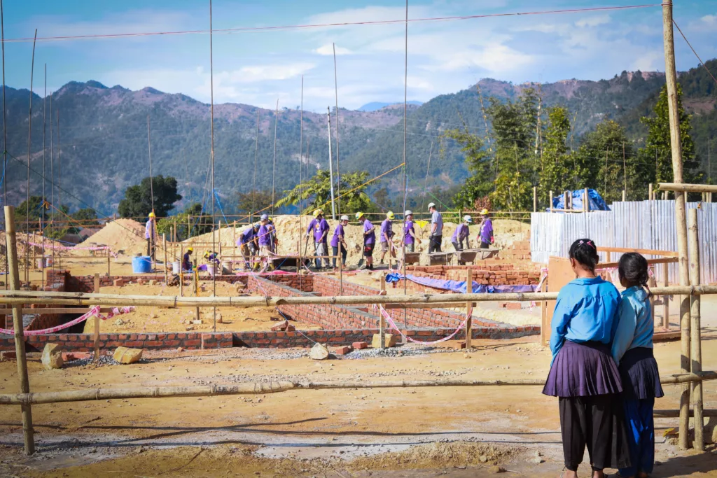 Two students in Nepal watch the construction of their new school