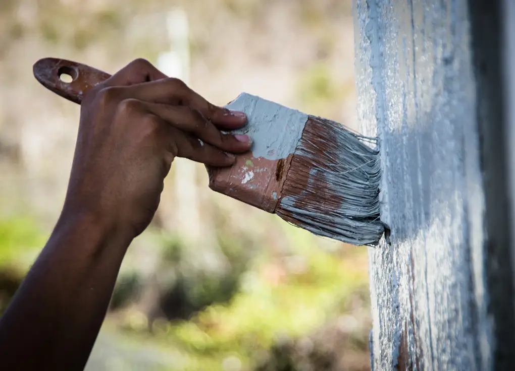 Primer plano de la pintura de una pared exterior. Se ven la mano, el pincel y la pared