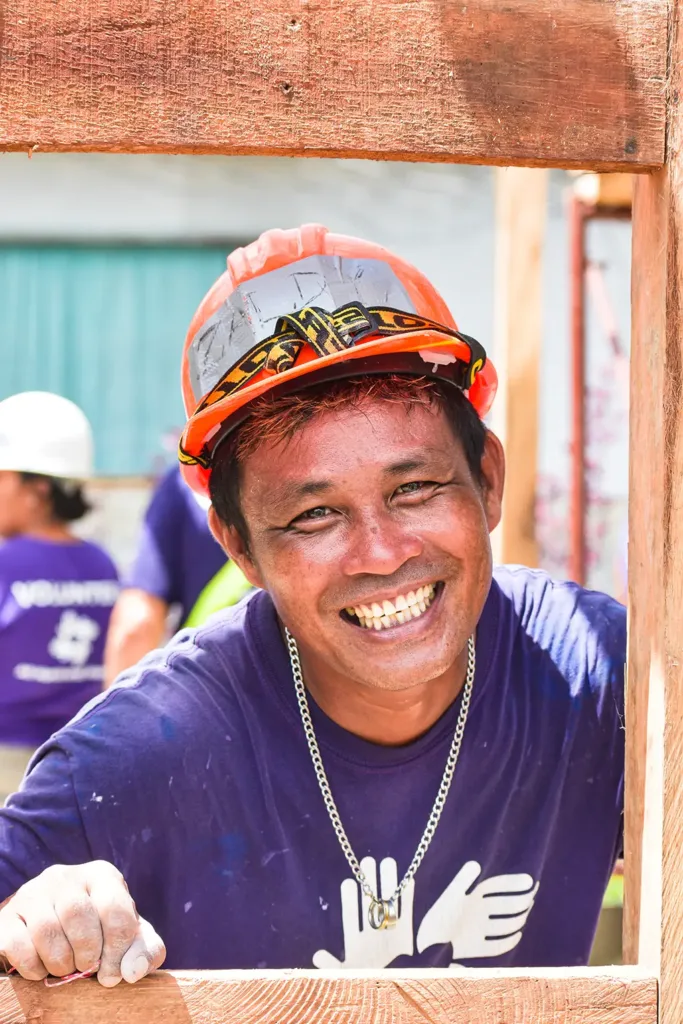 Voluntaria de AHAH sonriendo a través de una estructura de madera de la reconstrucción de una escuela
