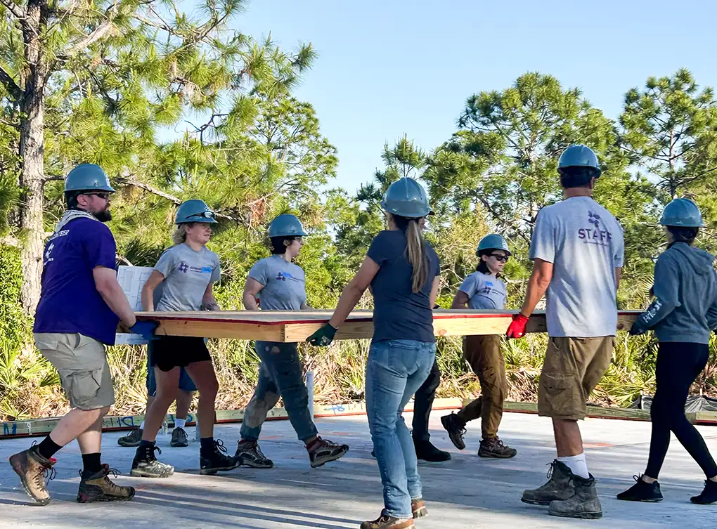 Grupo de voluntarios transportando un gran trozo de madera contrachapada